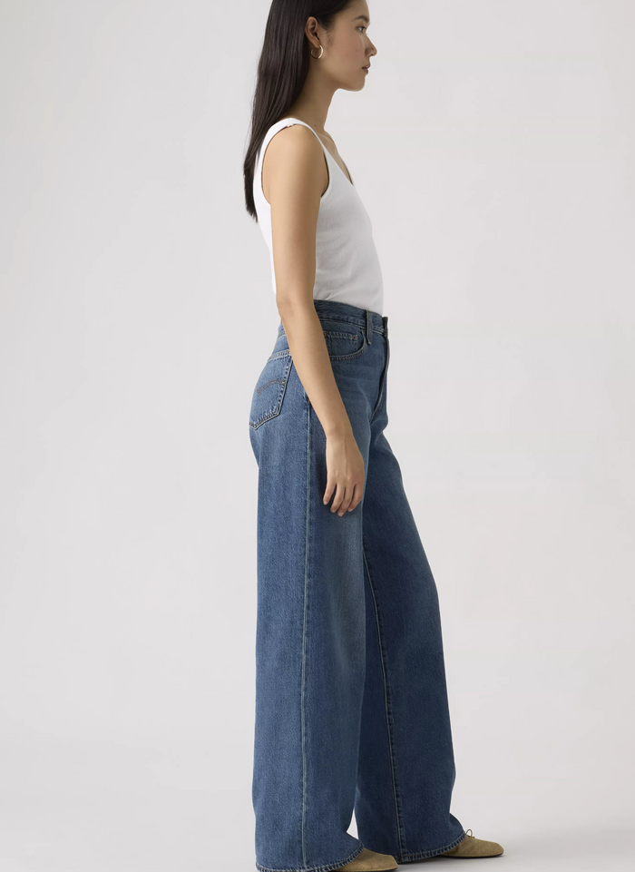 Woman wearing a white tank top and blue jeans on a plain background