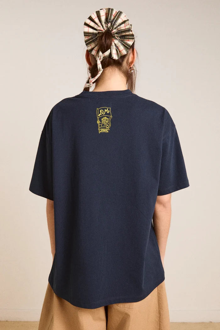 Person wearing a navy blue t-shirt with a logo on the back against a beige background
