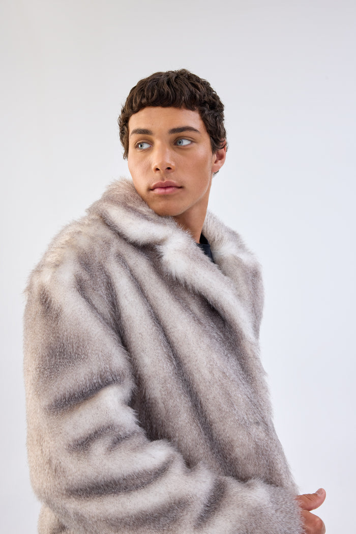 Close-up of a model wearing a grey faux fur coat with oversized notch lapel, looking off to the side