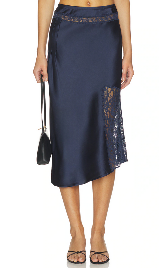 A navy blue satin midi skirt with black lace trim at the waist and a side slit, shown on a model holding a small black handbag against a white background.