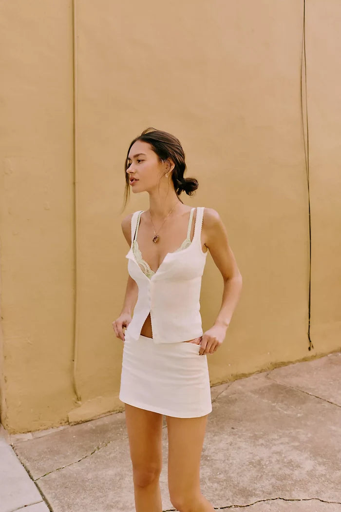 Woman wearing a Free People End Game Pointell tank in Sugar standing against a beige wall.