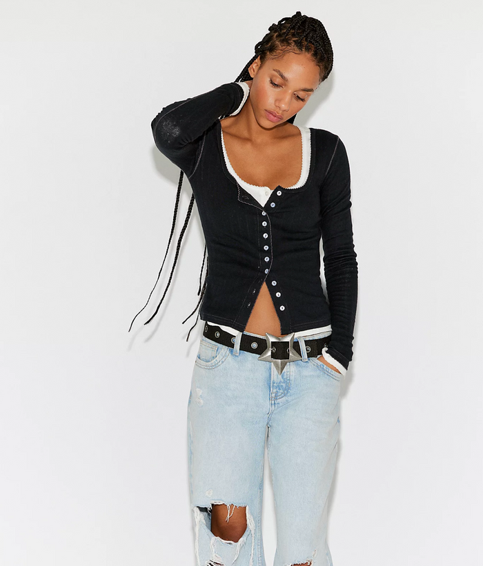 Woman wearing a black Free People End Game Pointelle Long Sleeve over a white shirt with light blue jeans on a white background