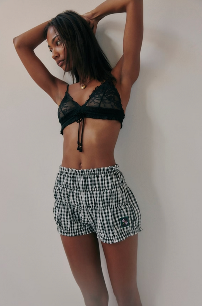 Woman wearing a black lace top and checkered shorts against a plain background