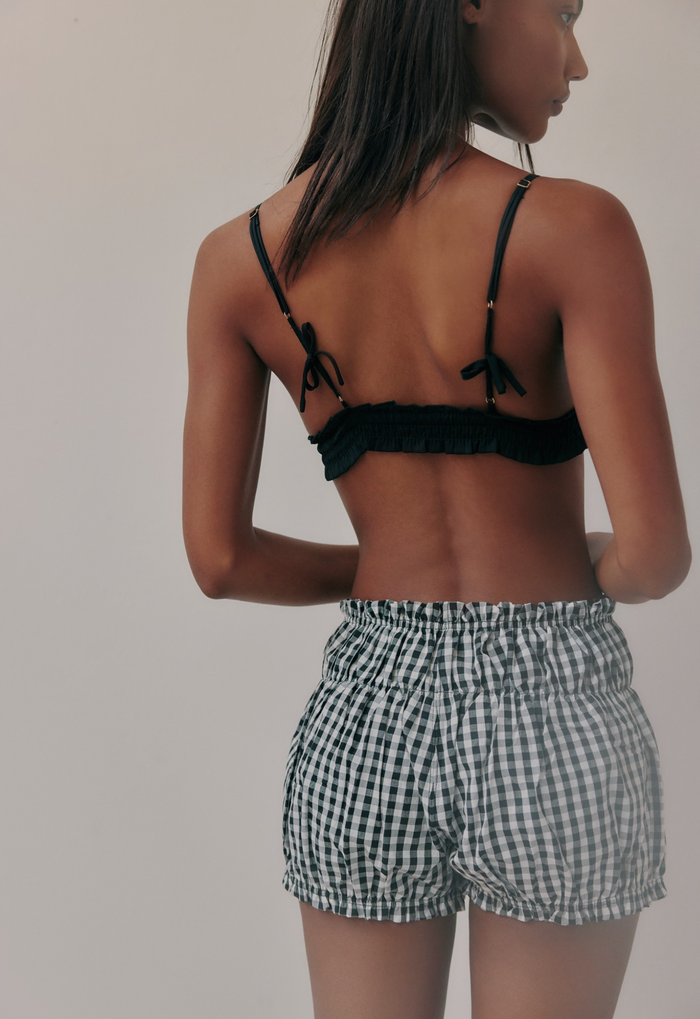 Woman wearing a black bikini top and checkered shorts on a plain background