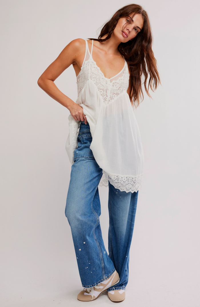 Woman wearing a ivory lace top and blue jeans on a plain background