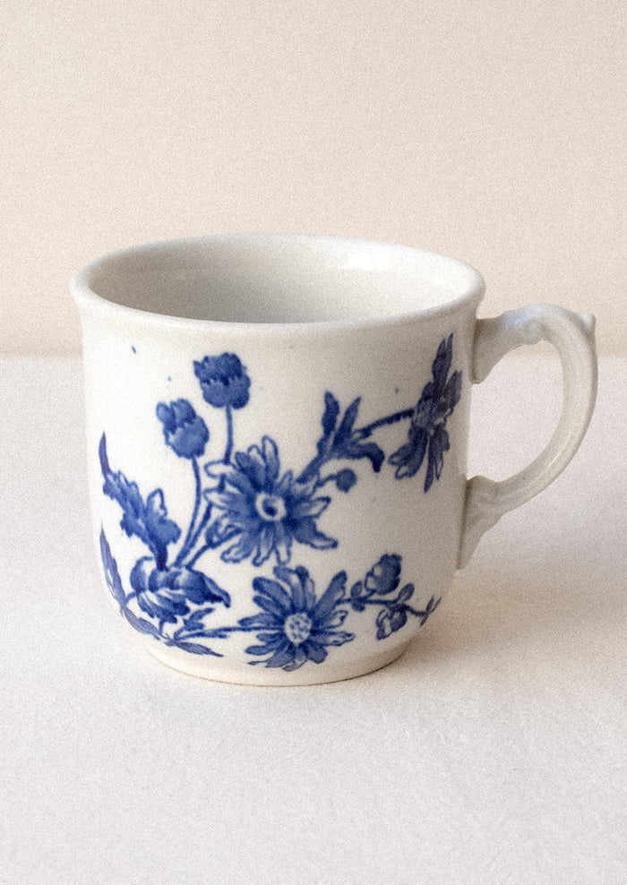 A white mug with flow blue floral pattern and ornate handle.