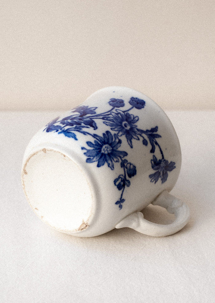 A white mug with flow blue floral pattern and ornate handle.