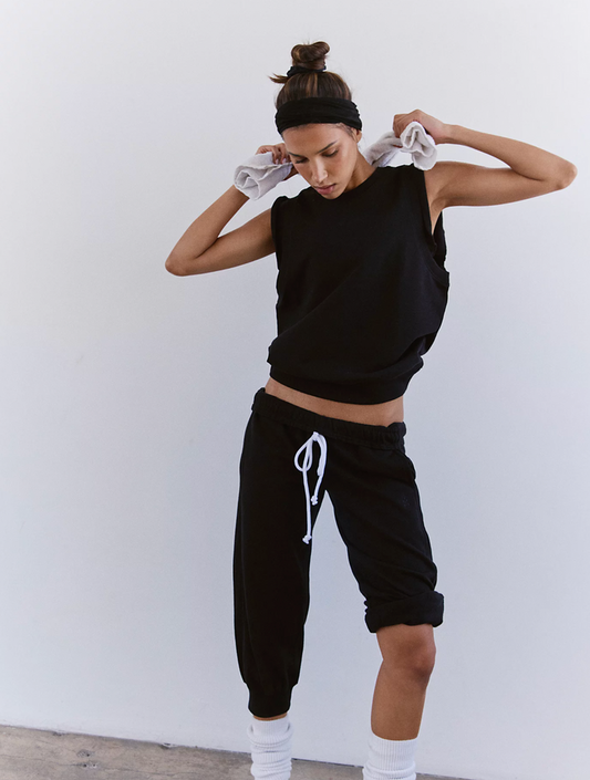 Woman in black sleeveless top and black jogger pants with white drawstring, standing against a white background.