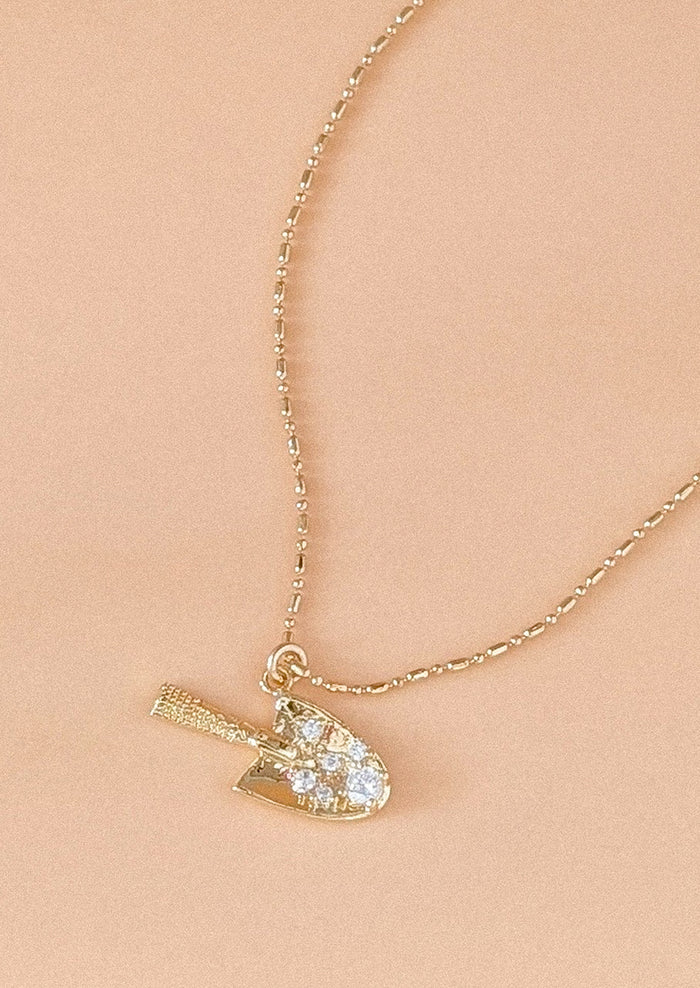 A gold necklace with garden trowel pendant charm.