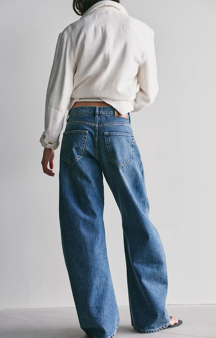 Person wearing blue jeans and a white sweater against a plain background