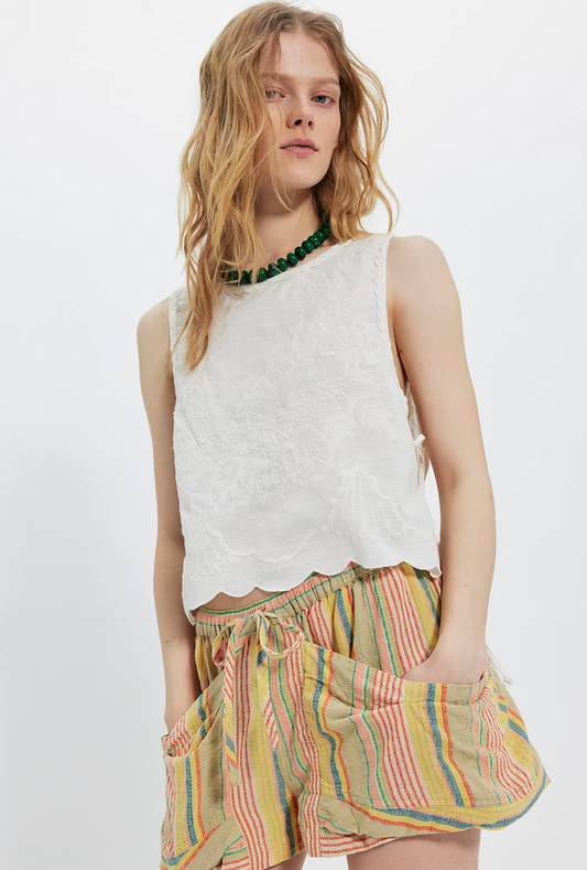 Woman wearing a white sleeveless top and colorful striped shorts on a white background