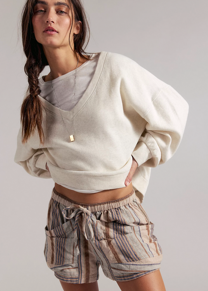 Woman wearing a beige oversized sweatshirt and striped shorts on a plain background