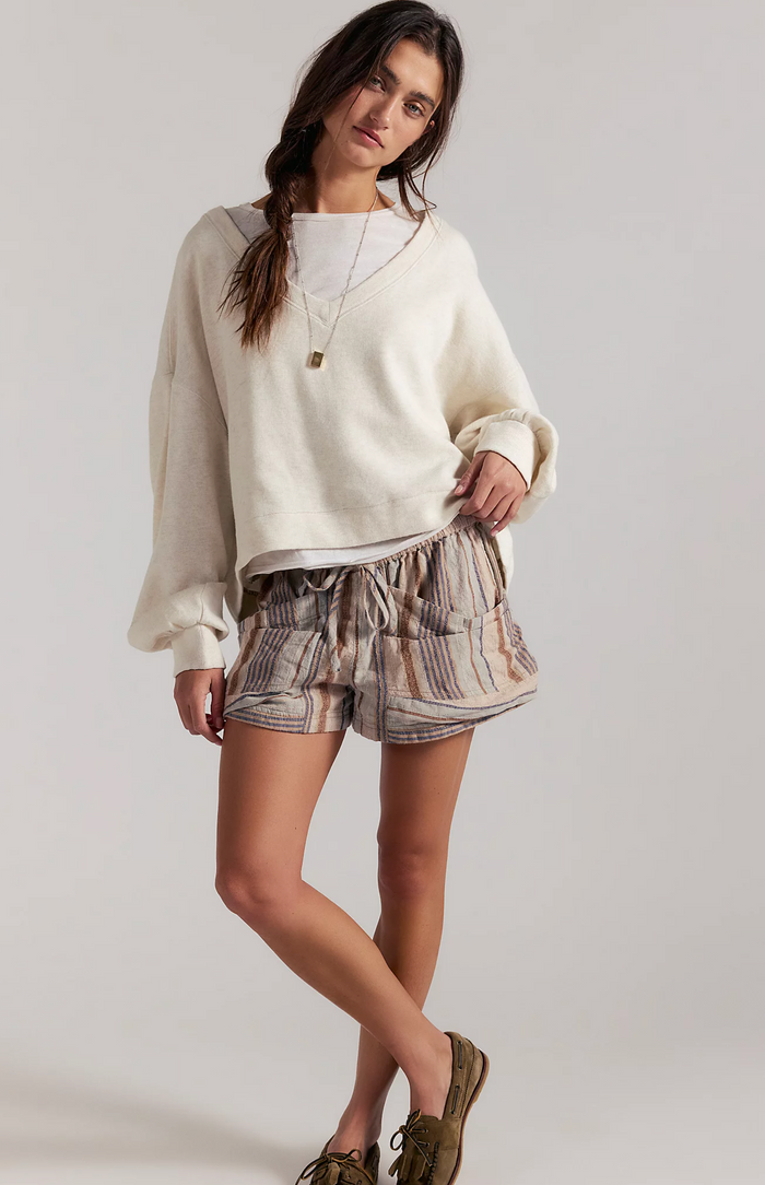 Woman wearing a white sweater and patterned shorts on a plain background