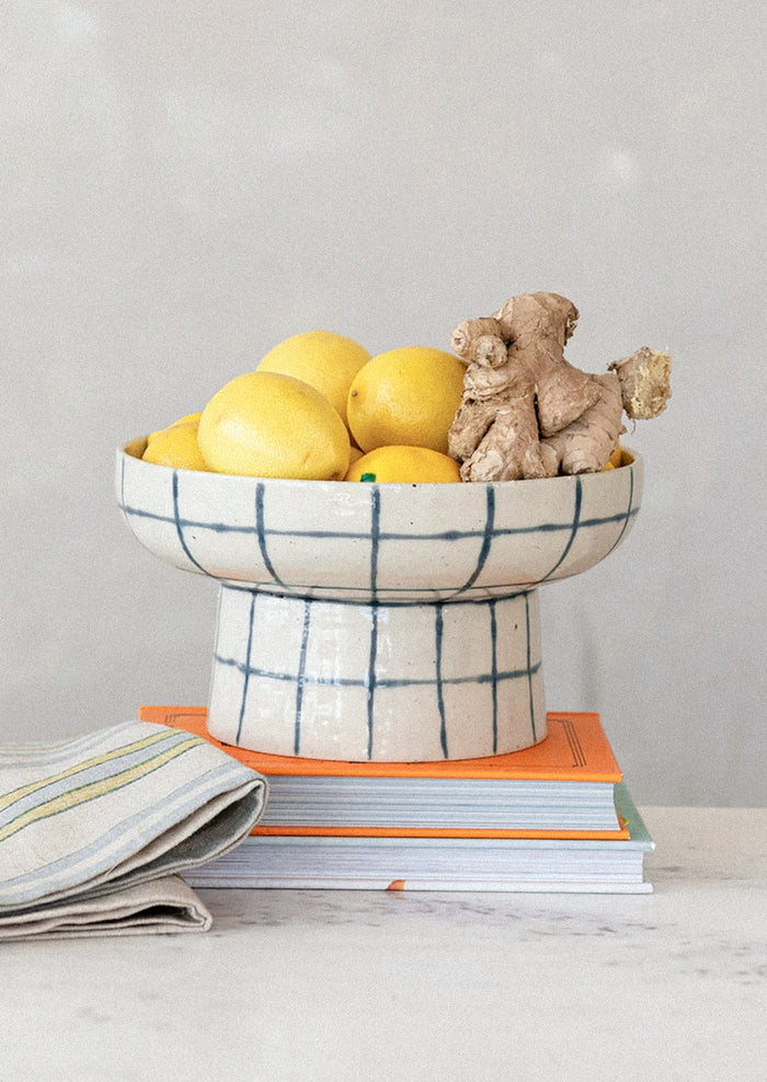 A footed pedestal bowl in natural ceramic with blue painted grid pattern.