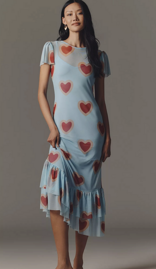 Woman wearing a light blue dress with red heart patterns against a gray background