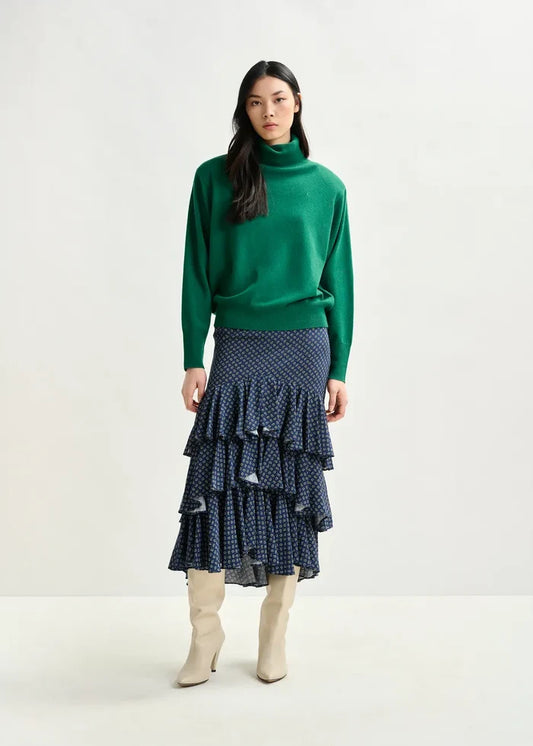 Woman wearing a green sweater and tiered navy skirt on a white background
