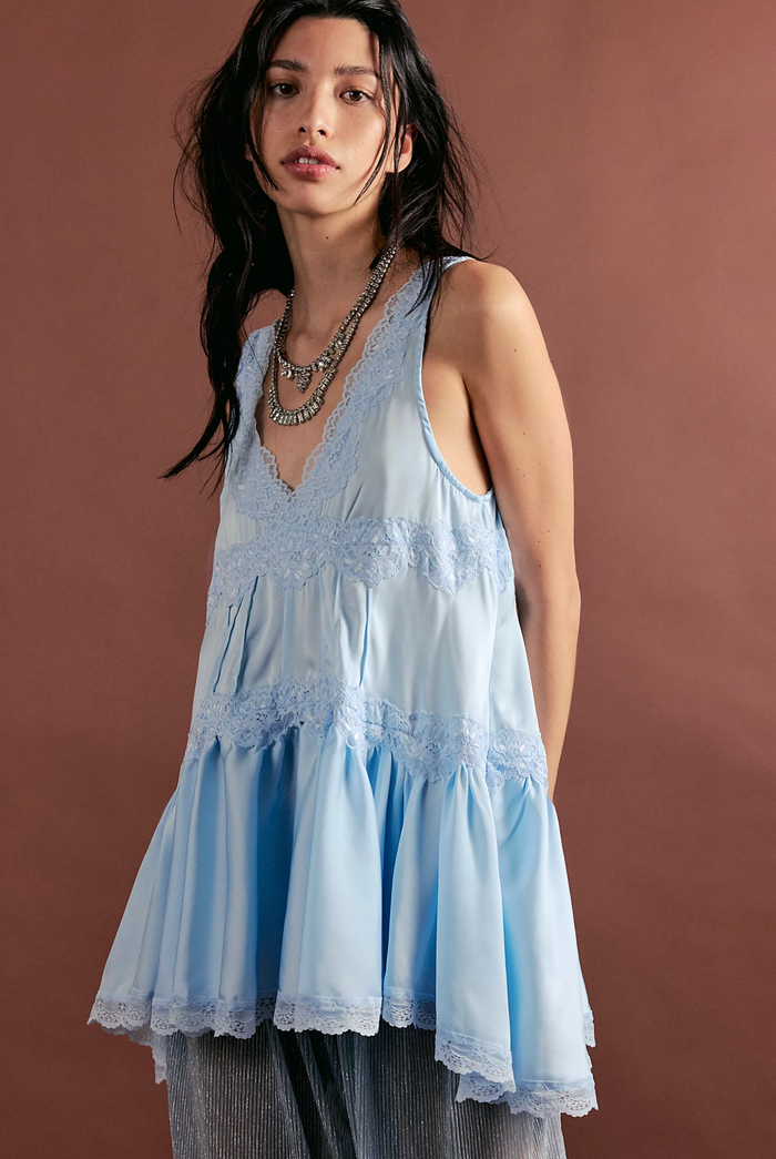 Woman wearing a dew shine colored lace dress against a brown background