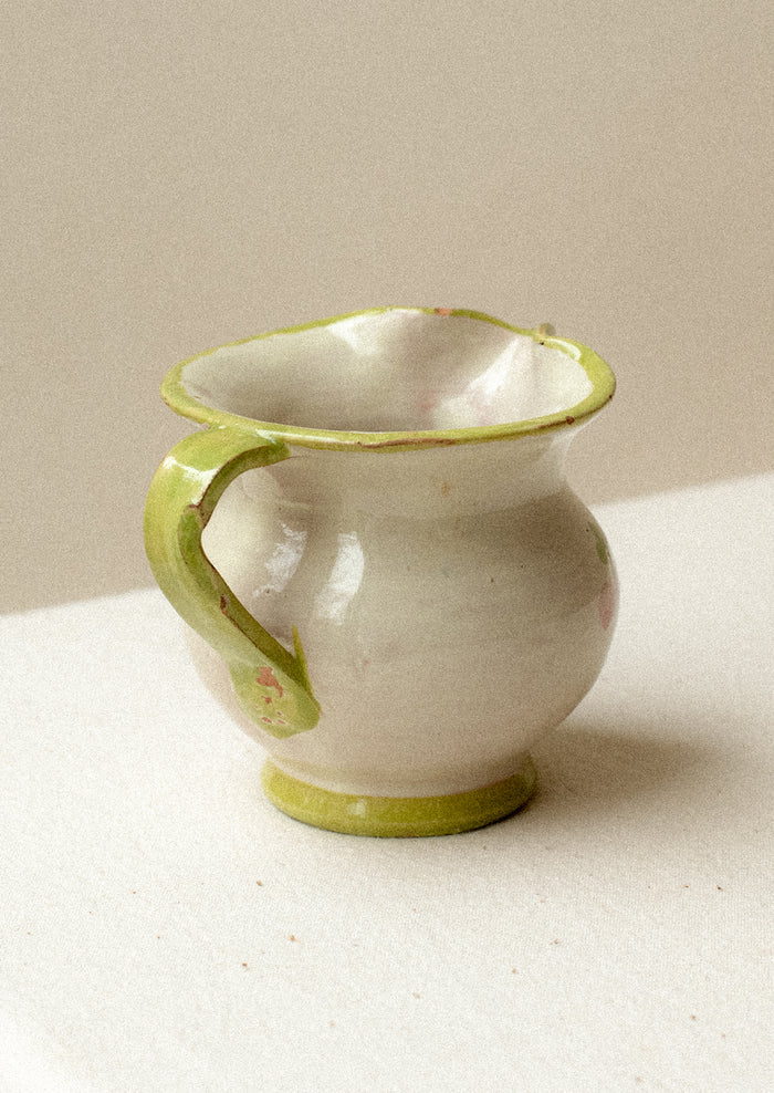 A small ceramic pitcher with painted floral design and green border.
