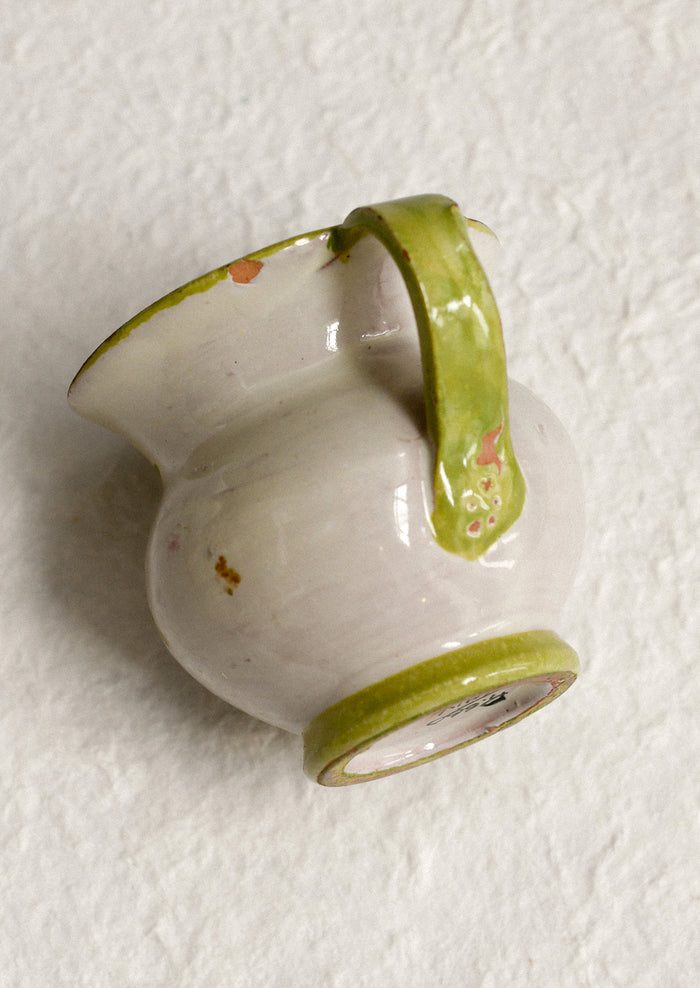 A small ceramic pitcher with painted floral design and green border.
