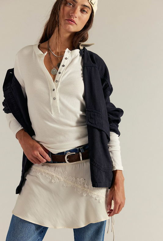 Woman wearing a ivory shirt, navy cardigan, and white skirt with lace details on a plain background
