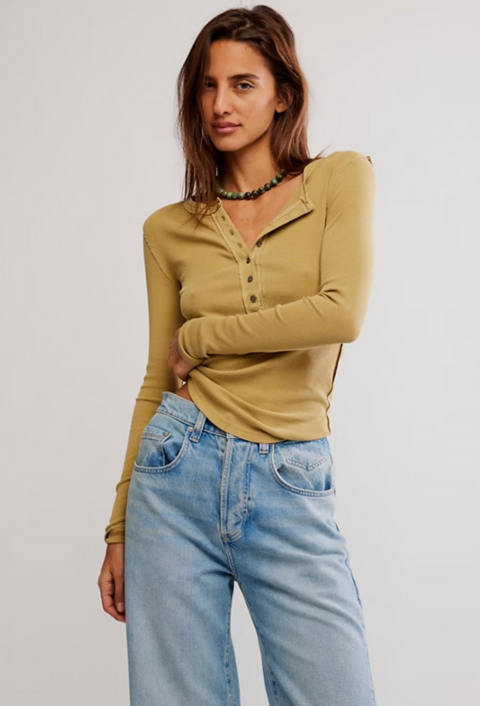 Woman wearing a tobacco long-sleeve top and light blue jeans on a plain background