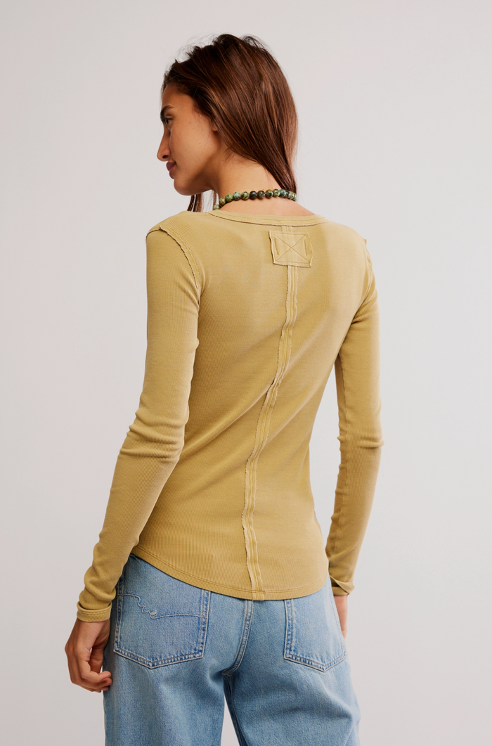 Woman wearing a tobacco long-sleeve top and blue jeans on a plain background