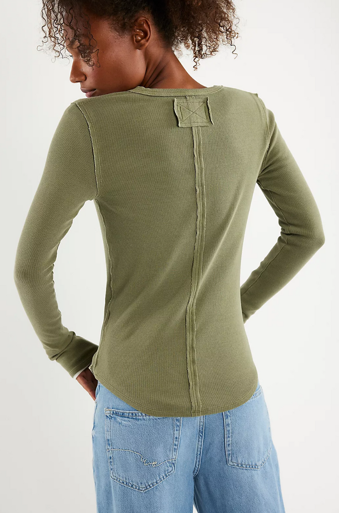 Person wearing a olive long-sleeve top with a plain background