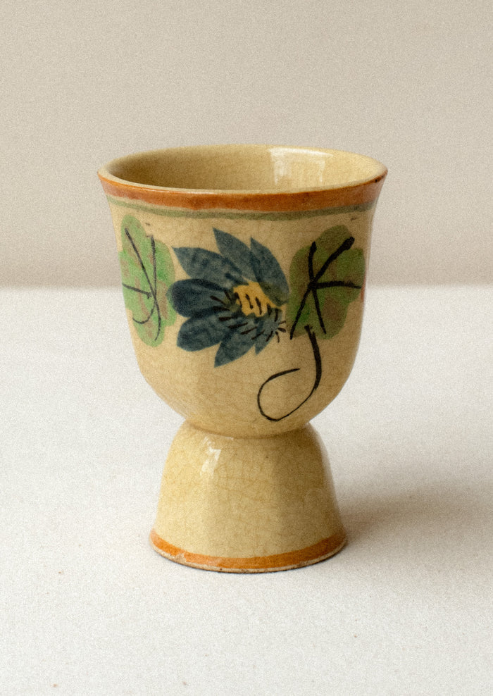 An antique egg cup in tan ceramic with caramel colored trim, and nasturtium floral pattern.