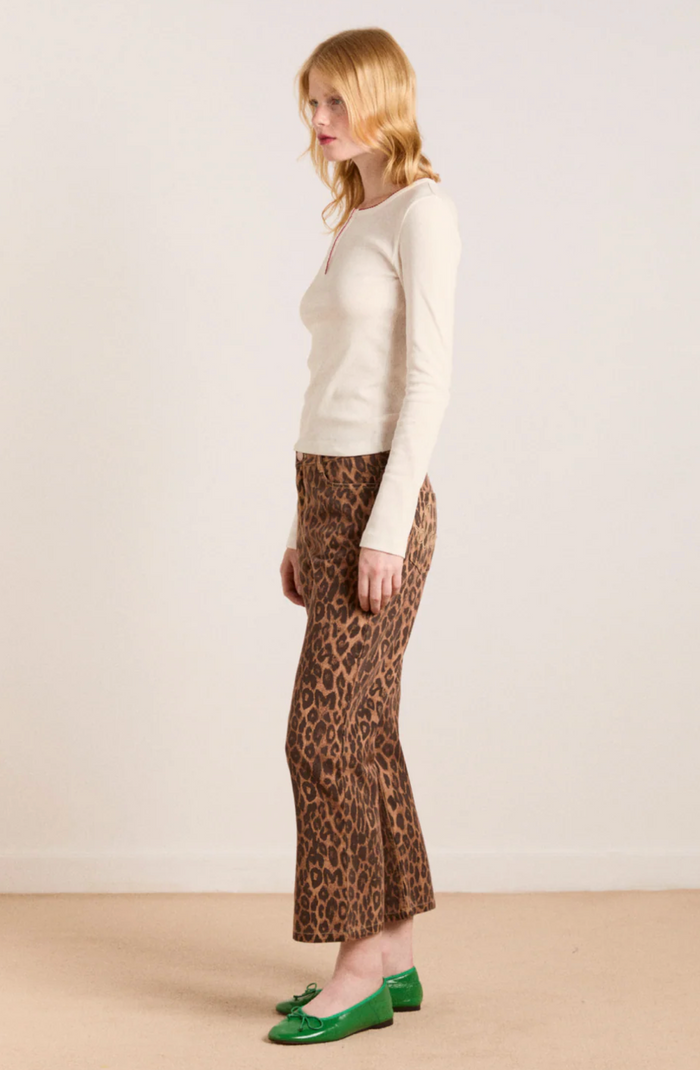 Woman wearing a cream sweater and leopard print pants against a plain background