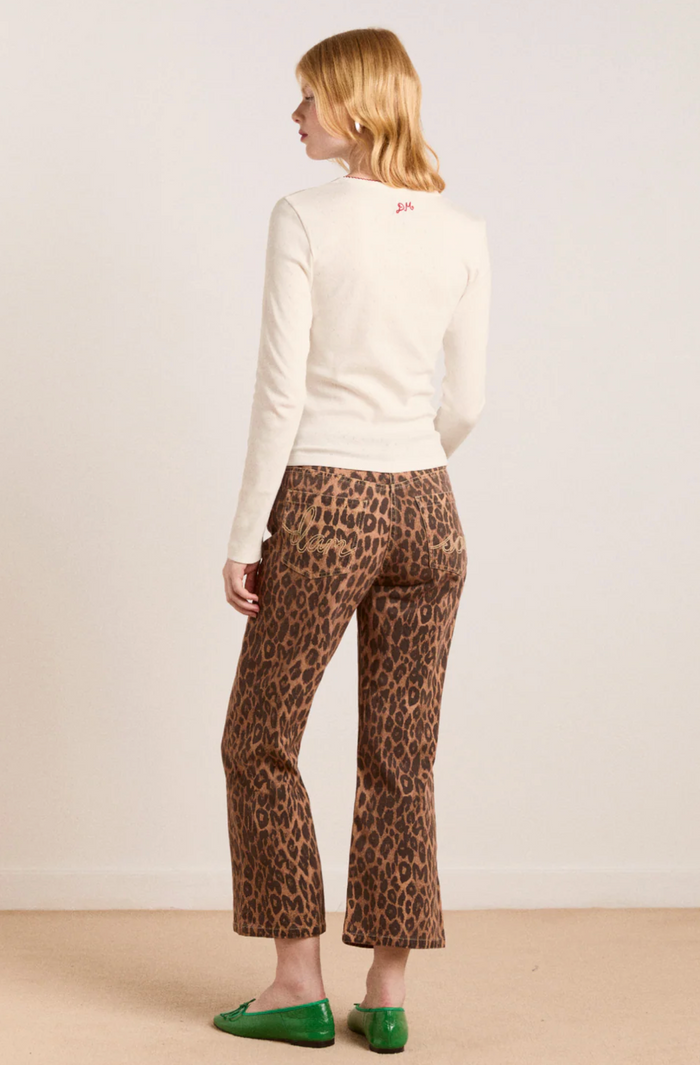 Woman wearing a white sweater and leopard print pants on a plain background