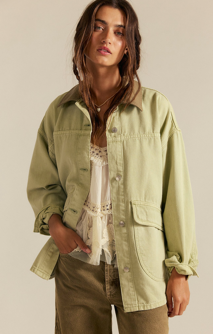 Woman wearing a washed sage jacket over a white top and brown pants on a beige background