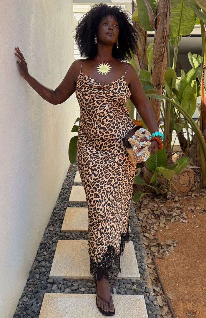 Woman in a leopard print dress with a scoop neck and adjustable straps standing outdoors with plants in the background