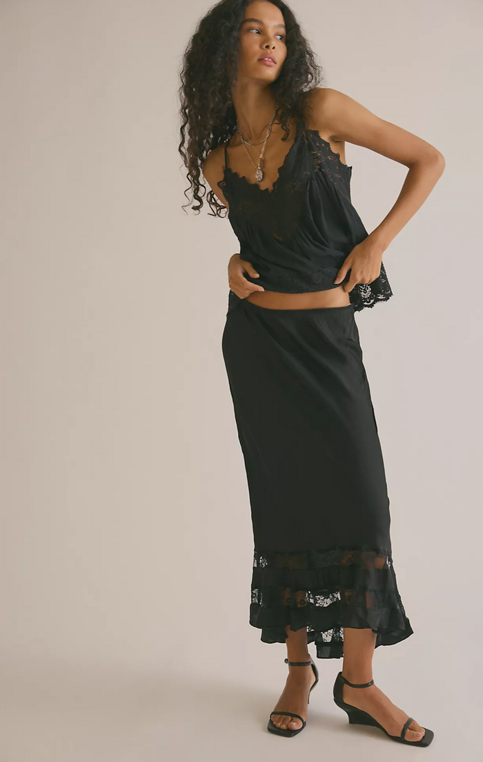 Woman wearing a black slip dress with floral lace details on a plain background