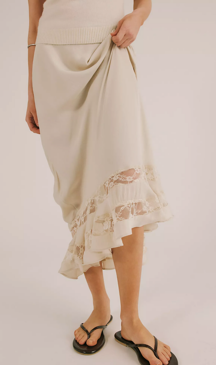 Person wearing a beige skirt with lace hem on a plain background