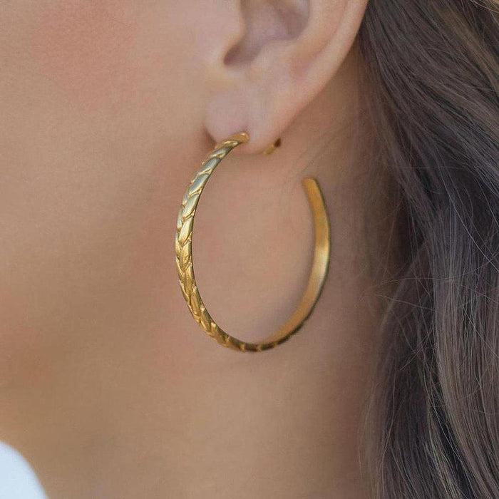 Gold hoop earrings with textured braided design, worn on ear.