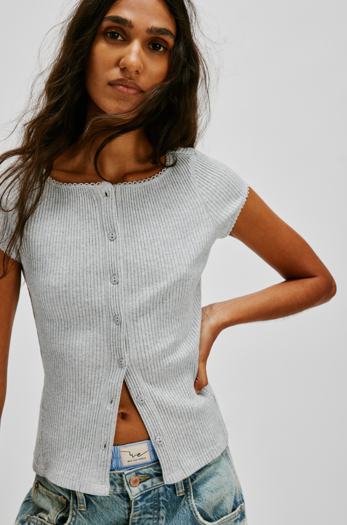 Woman wearing a light gray ribbed top and blue jeans on a white background