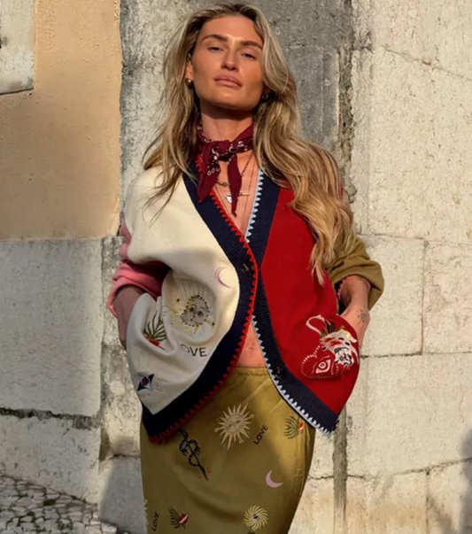 Woman wearing a colorful embroidered cardigan and skirt against a stone wall.