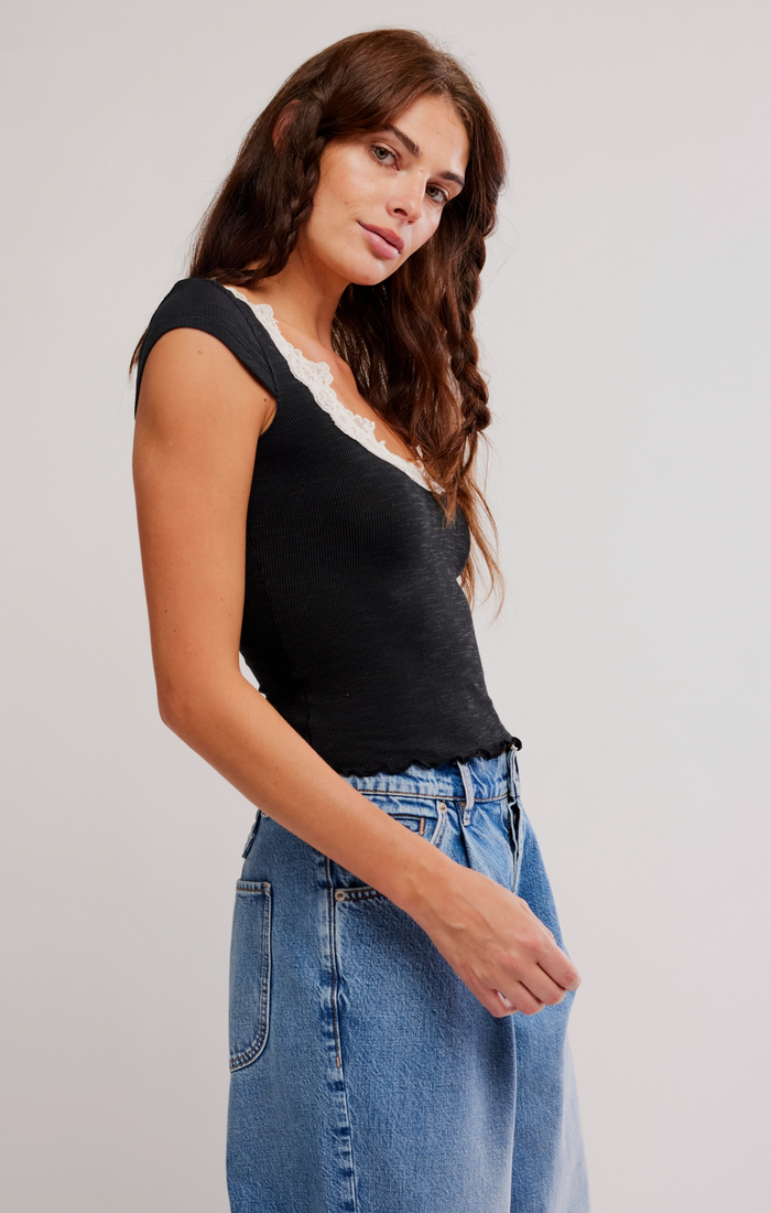 Woman wearing a black top with lace trim and blue jeans on a light gray background