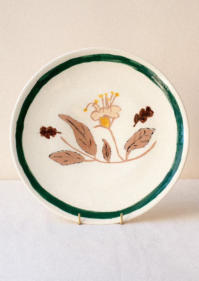 A ceramic plate with hand painted yellow and tan flower and green rim.