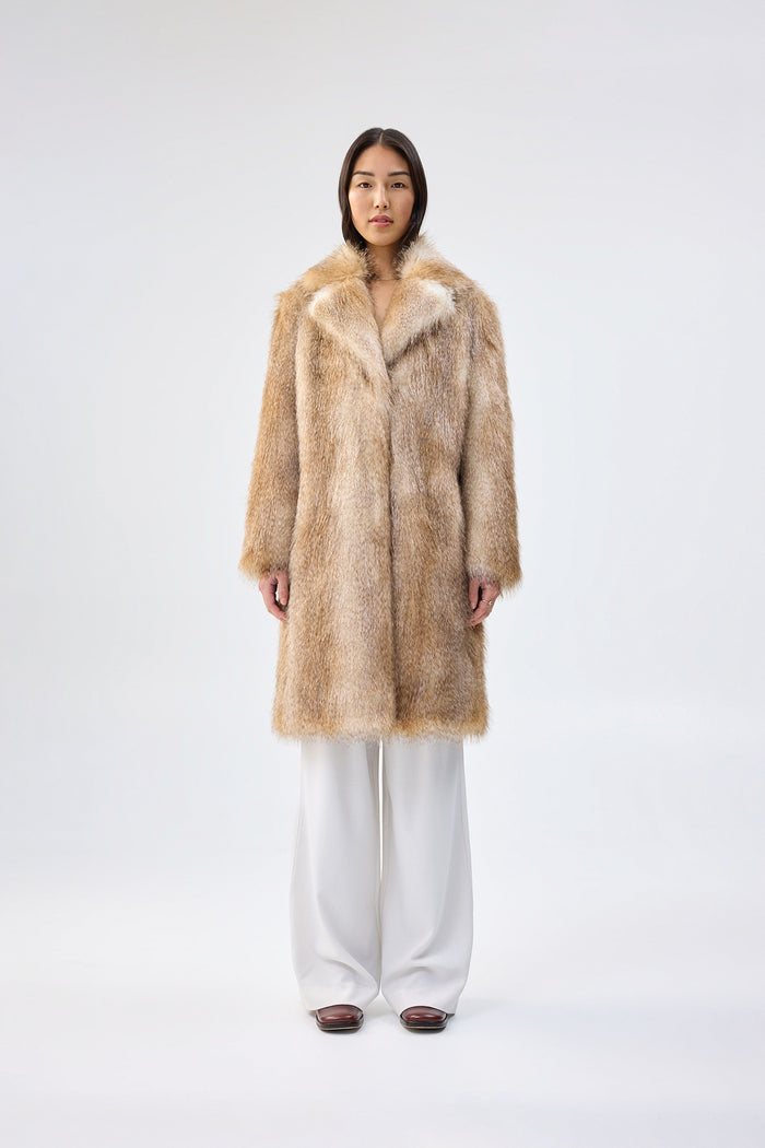 Light brown and cream faux fur coat with notch lapel and mid-length relaxed fit, worn over white wide-leg trousers, front view