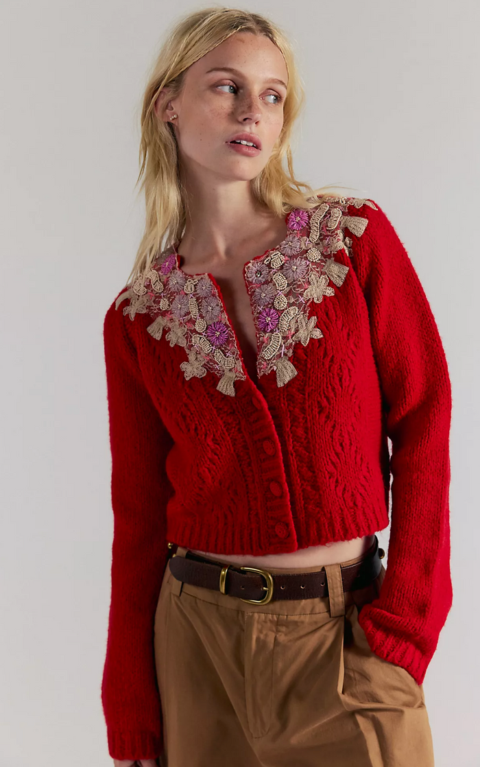 Woman wearing a red Cardigan sweater with floral embellishments on a plain background