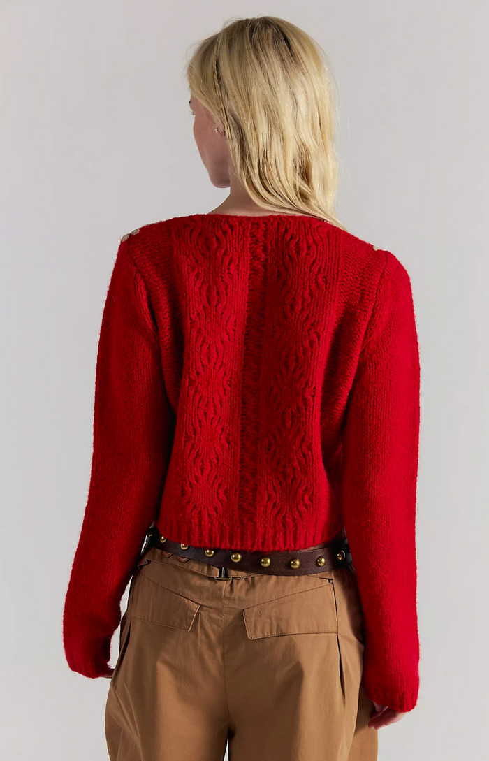 Person wearing a red knitted sweater and beige pants on a plain background
