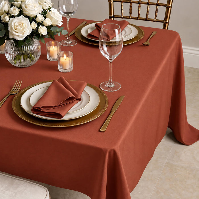 Terracotta rectangular tablecloth on a dining table set with plates and flowers.