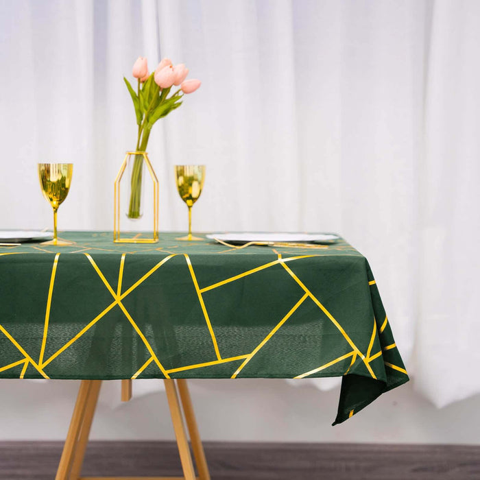 Green tablecloth with yellow geometric patterns, set with flowers and glasses.