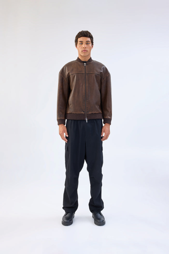 Brown vegan leather jacket with band collar and zip-front closure, cropped ribbed hem, worn over black cargo trousers, front view
