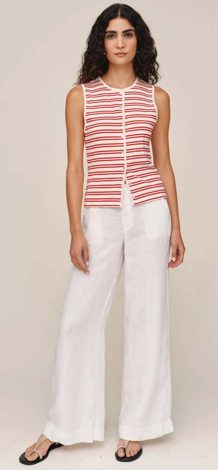 Woman wearing a red and white striped sleeveless top with white pants on a beige background
