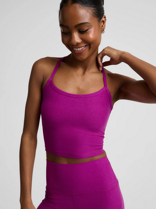 A woman wearing a bright berry bliss-colored athletic crop top and matching high-waisted leggings, shown from the chest down against a light gray studio background.