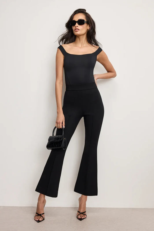 Woman wearing a black outfit with flared pants against a white background