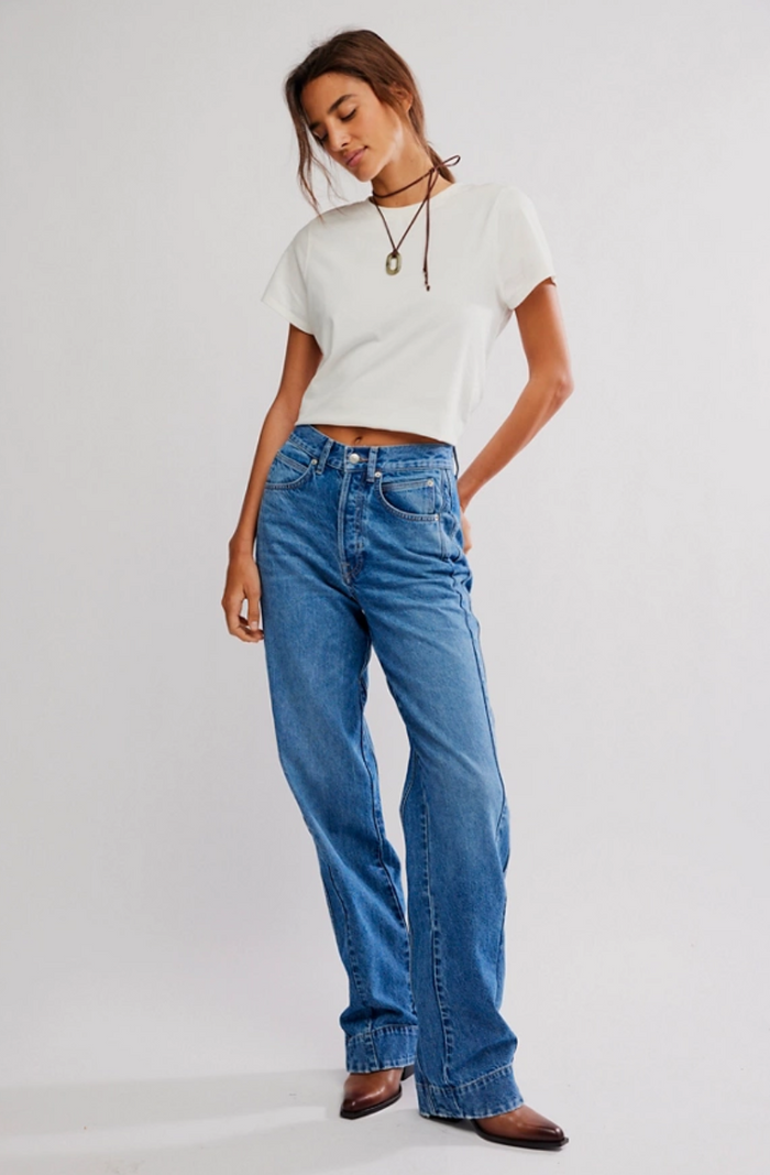 Woman wearing a white t-shirt and blue jeans on a plain background