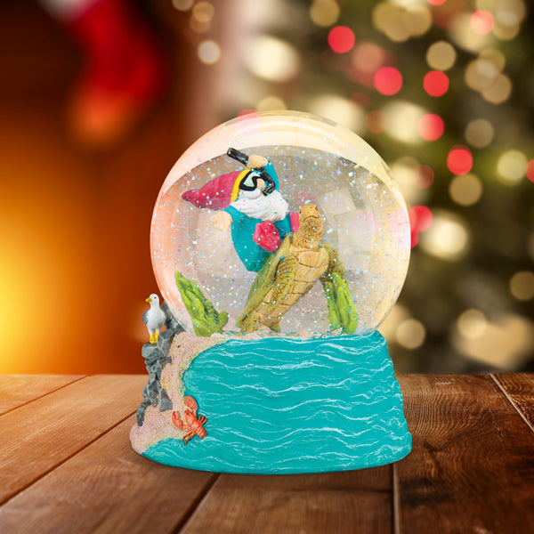 A snow globe with a parrot perched on a branch inside, atop a blue ocean-themed base with a seagull and starfish. The background is blurred with warm lights and a festive atmosphere.